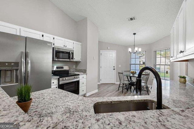 kitchen with visible vents, vaulted ceiling, stainless steel appliances, white cabinetry, and a sink