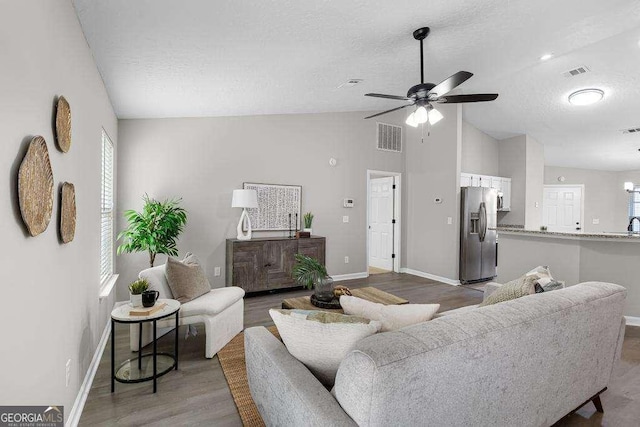 living room featuring lofted ceiling, wood finished floors, visible vents, and a textured ceiling