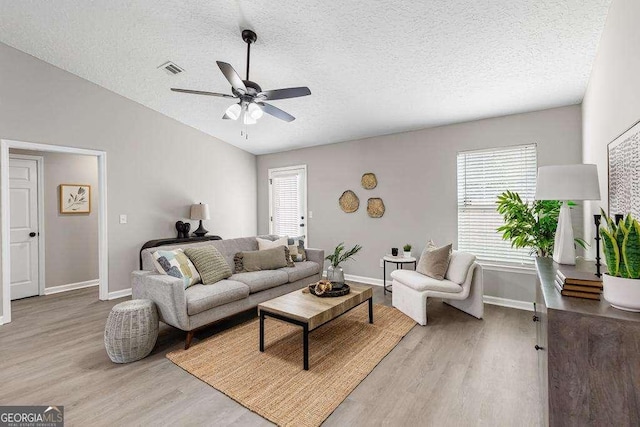 living room featuring a textured ceiling, visible vents, light wood finished floors, and ceiling fan