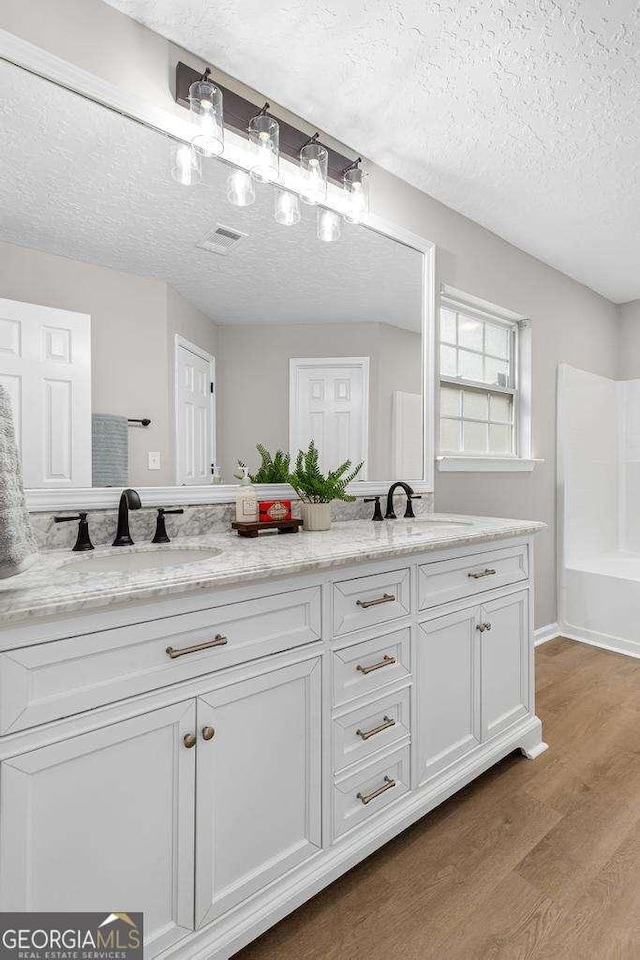 bathroom with visible vents, a sink, a textured ceiling, wood finished floors, and double vanity