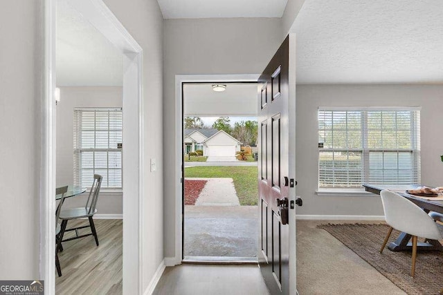 doorway to outside with a textured ceiling, baseboards, and wood finished floors