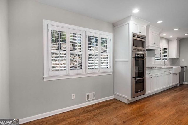 kitchen featuring wood finished floors, baseboards, visible vents, appliances with stainless steel finishes, and white cabinetry