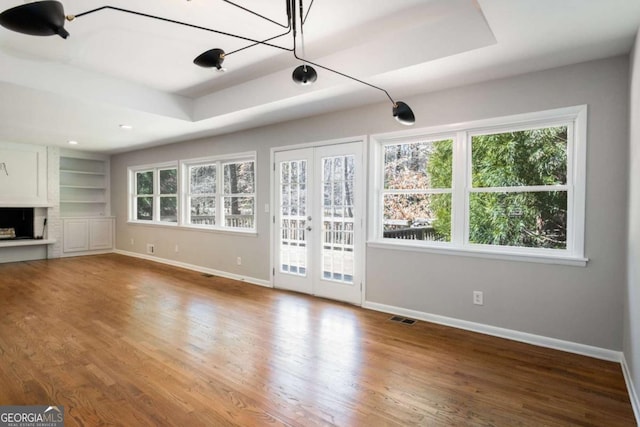 unfurnished living room featuring visible vents, wood finished floors, french doors, baseboards, and a raised ceiling