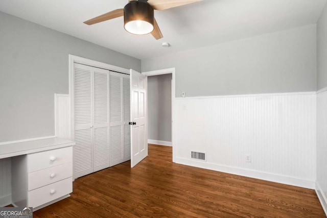 unfurnished bedroom with visible vents, wood finished floors, a closet, wainscoting, and ceiling fan