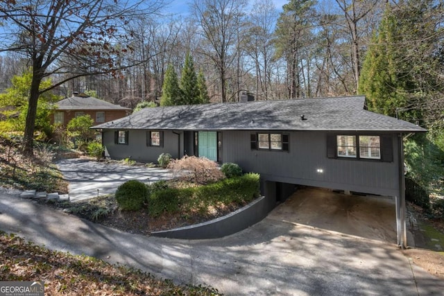 ranch-style home with concrete driveway, a carport, a chimney, and a shingled roof