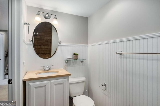 half bathroom with vanity, wainscoting, and toilet