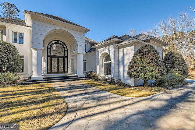 entrance to property featuring french doors, a lawn, and stucco siding