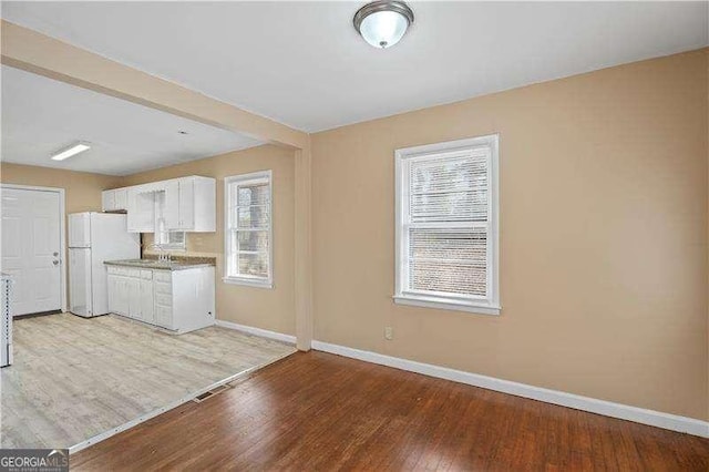 kitchen featuring baseboards, light wood-style flooring, freestanding refrigerator, white cabinetry, and a sink