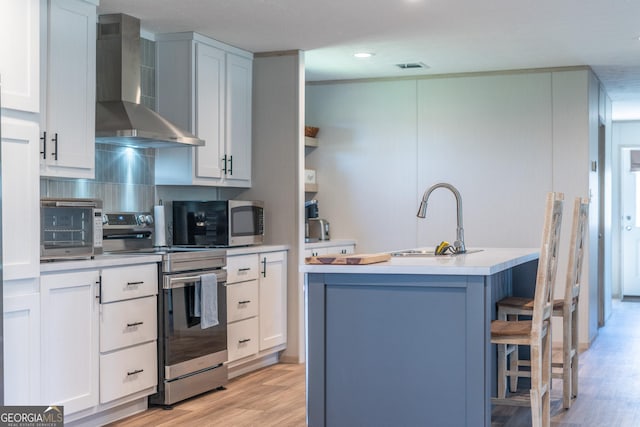4159 Folks Dr, Blackshear, GA 31516 - kitchen with light wood-type flooring, an island with sink, a sink, stainless steel appliances, and wall chimney range hood