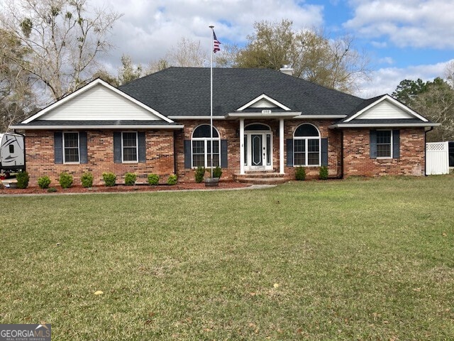 ranch-style home with a front yard, brick siding, and roof with shingles