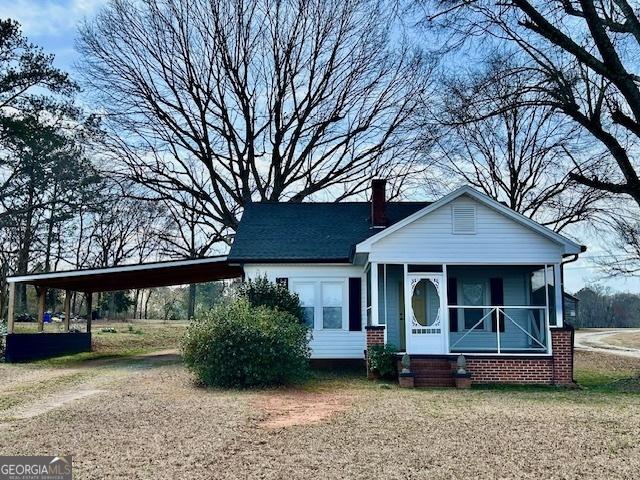 bungalow-style house featuring a carport, a chimney, driveway, and a sunroom