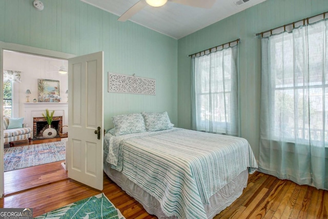 bedroom with a fireplace, wood finished floors, visible vents, and a ceiling fan