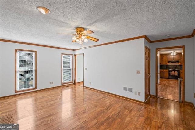 spare room featuring visible vents, baseboards, ceiling fan, ornamental molding, and wood finished floors