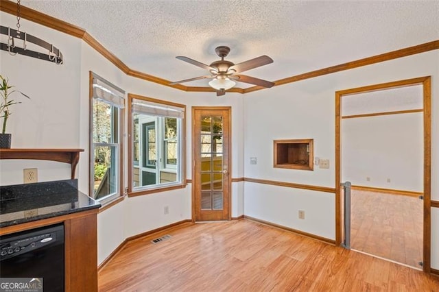 unfurnished dining area with a textured ceiling, light wood-style floors, crown molding, baseboards, and ceiling fan