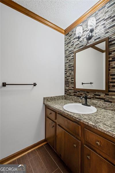 bathroom featuring a textured ceiling, vanity, crown molding, baseboards, and wood tiled floor