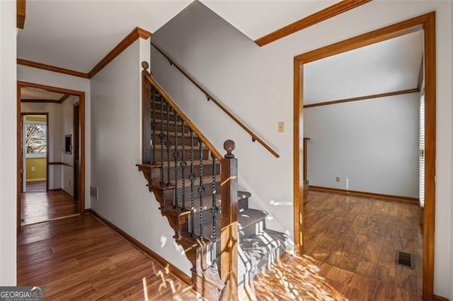 staircase featuring crown molding, wood finished floors, baseboards, and visible vents