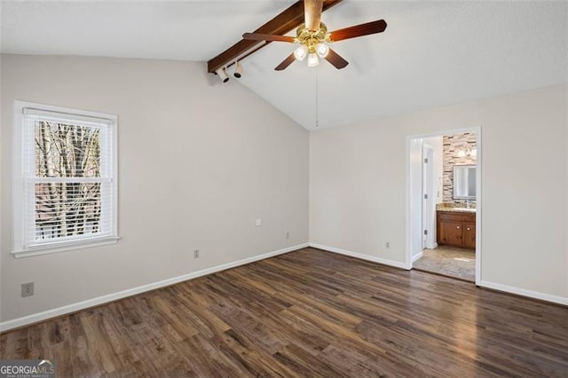 unfurnished bedroom featuring ceiling fan, baseboards, lofted ceiling with beams, ensuite bathroom, and dark wood-style flooring