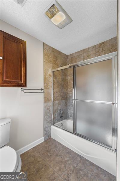 full bathroom featuring visible vents, enclosed tub / shower combo, toilet, and a textured ceiling