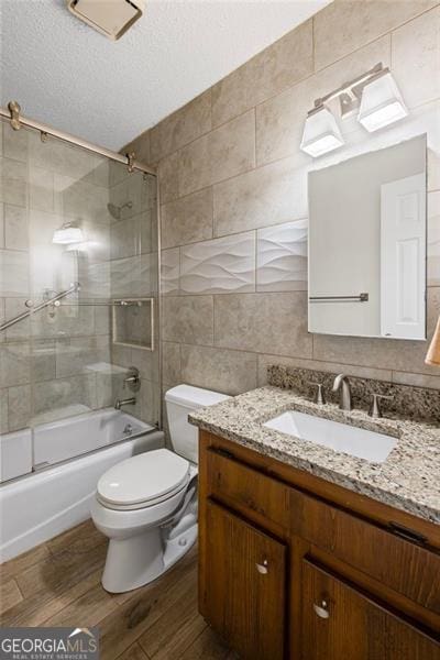 full bathroom with tile walls, vanity, wood finished floors, combined bath / shower with glass door, and a textured ceiling