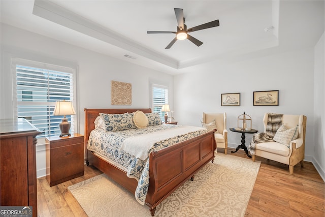 bedroom with visible vents, a raised ceiling, baseboards, and light wood-style flooring