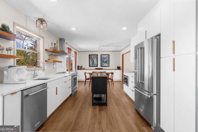 kitchen featuring open shelves, premium appliances, a sink, white cabinets, and wall chimney range hood