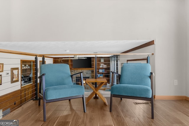 living area with a stone fireplace, visible vents, baseboards, and wood finished floors