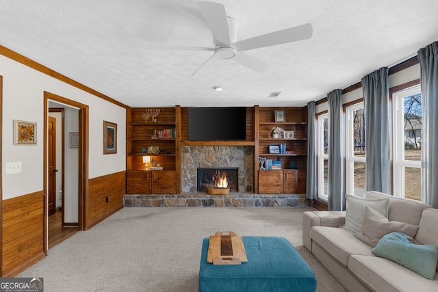 living area featuring wooden walls, built in shelves, a stone fireplace, wainscoting, and a textured ceiling