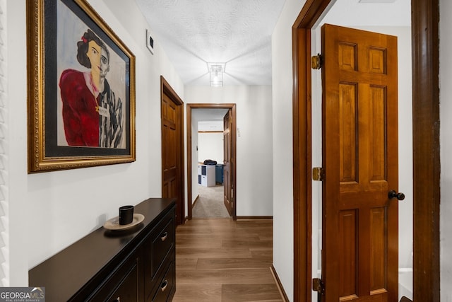 corridor featuring visible vents, baseboards, a textured ceiling, and wood finished floors