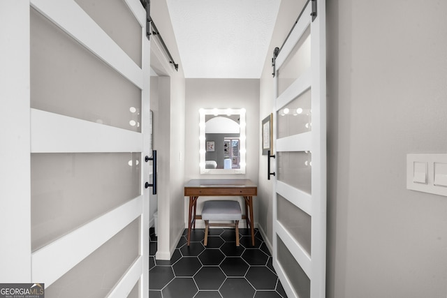 hallway featuring a barn door, a textured ceiling, and dark tile patterned floors