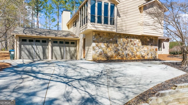 view of side of property featuring stone siding, driveway, a chimney, and a garage