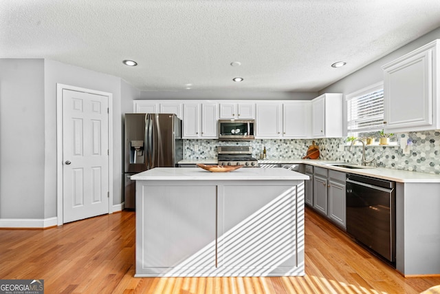 kitchen with light wood-type flooring, light countertops, decorative backsplash, stainless steel appliances, and a sink