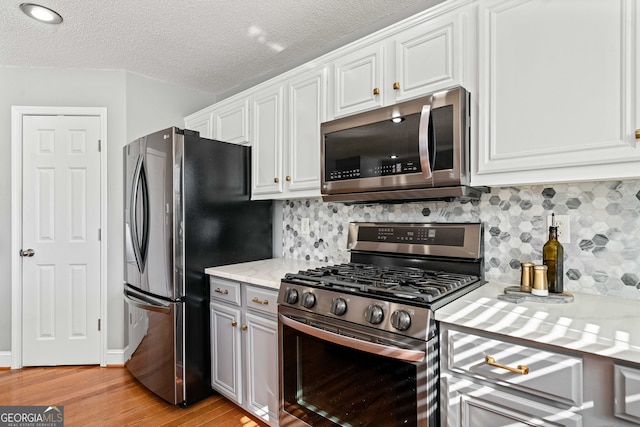 kitchen featuring backsplash, a textured ceiling, stainless steel appliances, white cabinets, and light wood finished floors