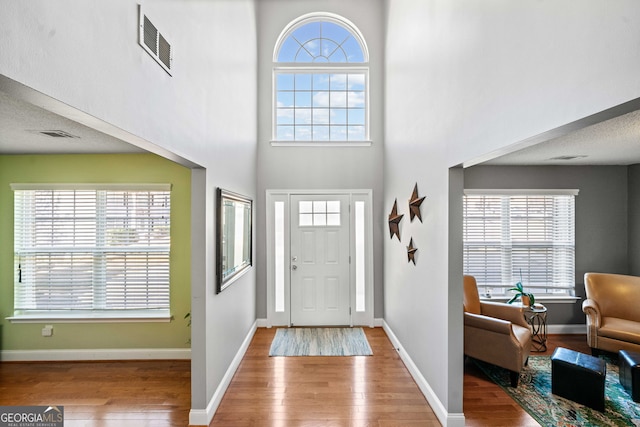 entryway with visible vents, baseboards, wood finished floors, and a towering ceiling