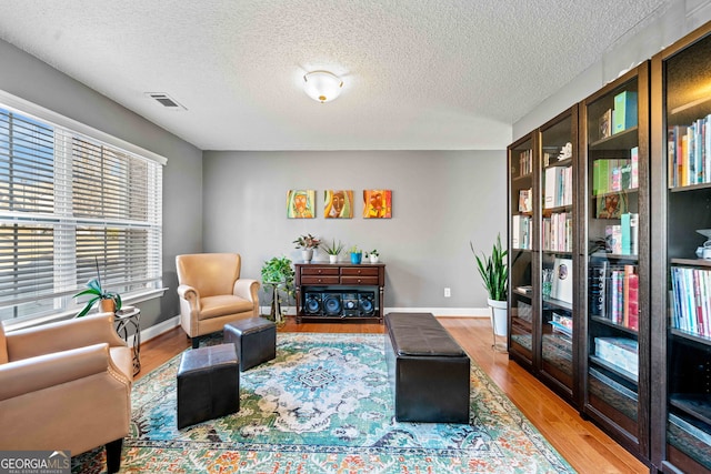 living area featuring visible vents, a textured ceiling, baseboards, and wood finished floors