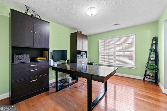 office space featuring a textured ceiling, light wood-style floors, visible vents, and baseboards