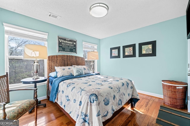 bedroom featuring hardwood / wood-style flooring, baseboards, visible vents, and a textured ceiling