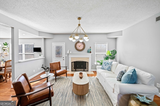 living room with visible vents, a notable chandelier, a textured ceiling, a premium fireplace, and baseboards