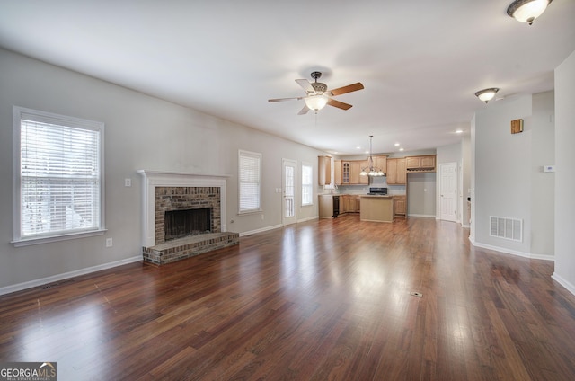 unfurnished living room with visible vents, a ceiling fan, baseboards, a brick fireplace, and dark wood-style flooring