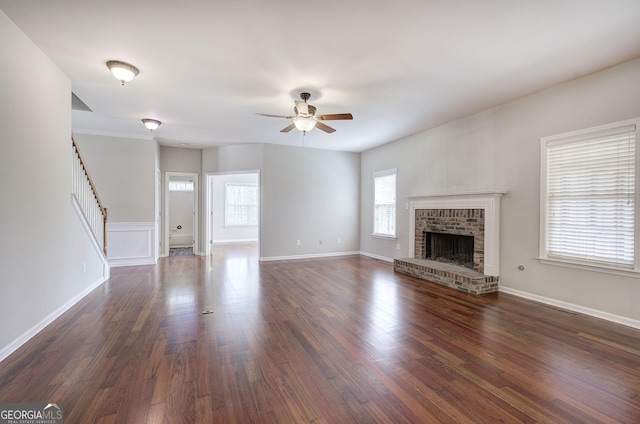 unfurnished living room with dark wood-style flooring, a fireplace, baseboards, ceiling fan, and stairs