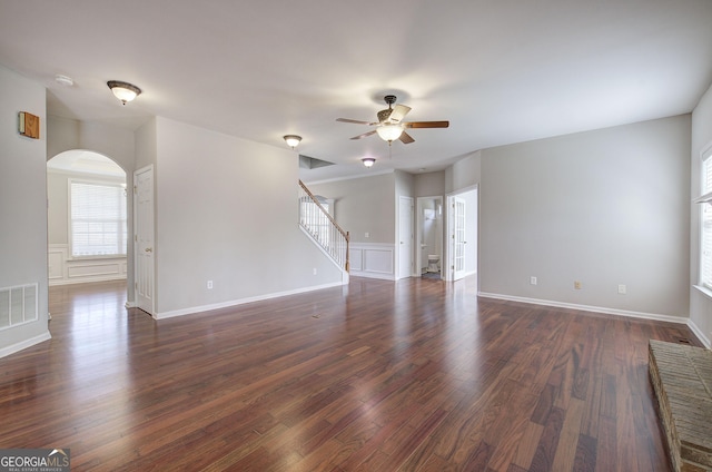 unfurnished living room with visible vents, stairway, arched walkways, dark wood-style floors, and a ceiling fan