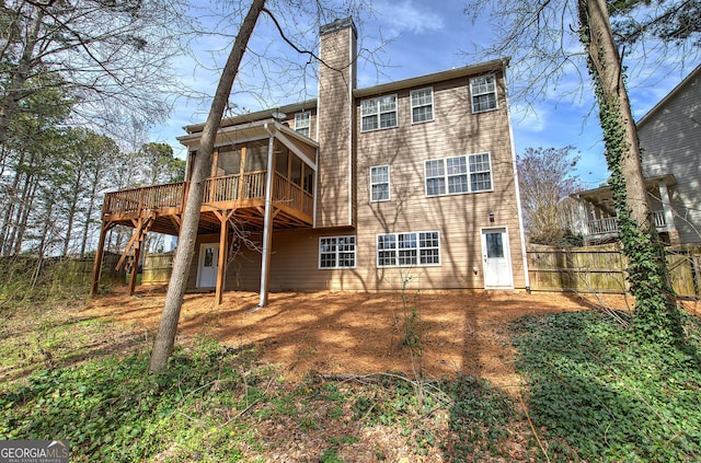 rear view of house featuring a deck, fence, a sunroom, and a chimney