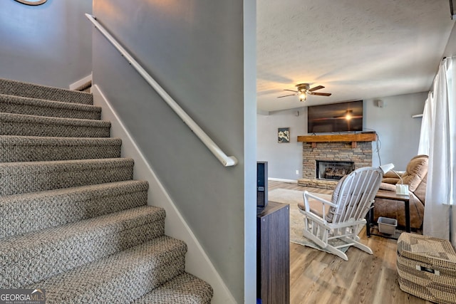95 Volunteer Ln, Murphy, NC 28906 - stairway featuring a ceiling fan, a textured ceiling, wood finished floors, a stone fireplace, and baseboards