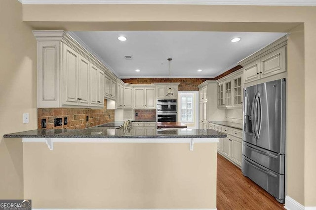 kitchen featuring dark wood-style floors, visible vents, a peninsula, stainless steel appliances, and glass insert cabinets