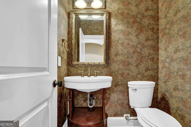 half bath featuring a sink, toilet, and wallpapered walls