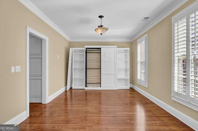 unfurnished bedroom with visible vents, baseboards, wood finished floors, and crown molding