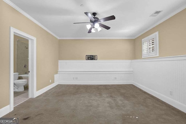 empty room with visible vents, carpet floors, wainscoting, crown molding, and ceiling fan