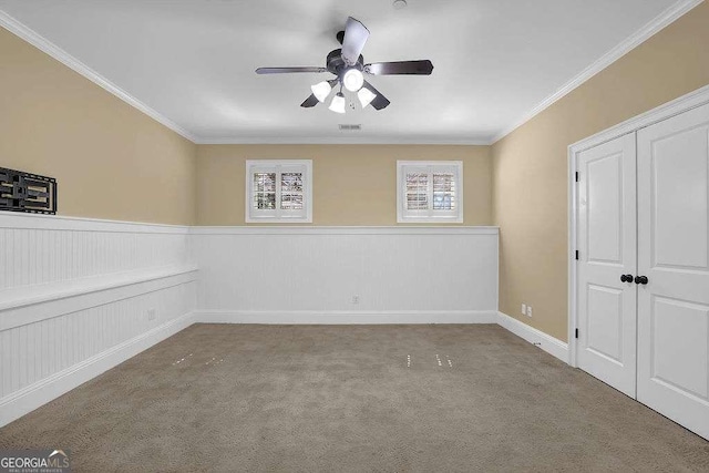 empty room with a wainscoted wall, visible vents, ornamental molding, and carpet flooring