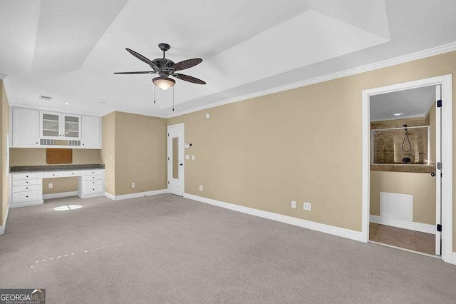 unfurnished living room featuring ceiling fan, baseboards, ornamental molding, light carpet, and built in desk