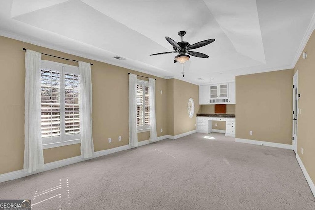 unfurnished living room featuring built in desk, plenty of natural light, a raised ceiling, and visible vents