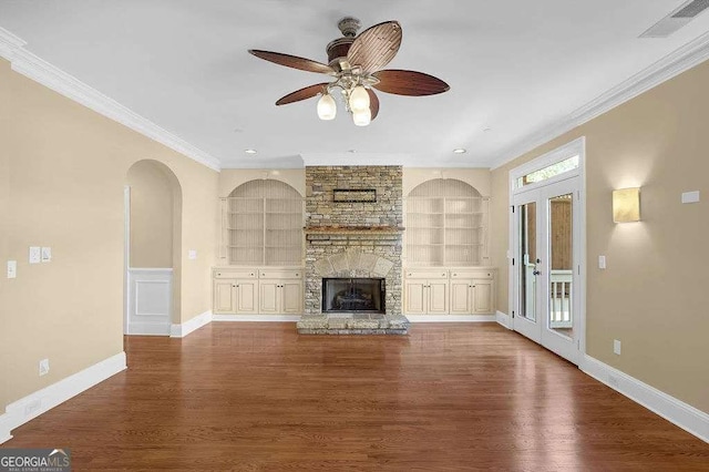 unfurnished living room with built in shelves, a stone fireplace, dark wood finished floors, and crown molding